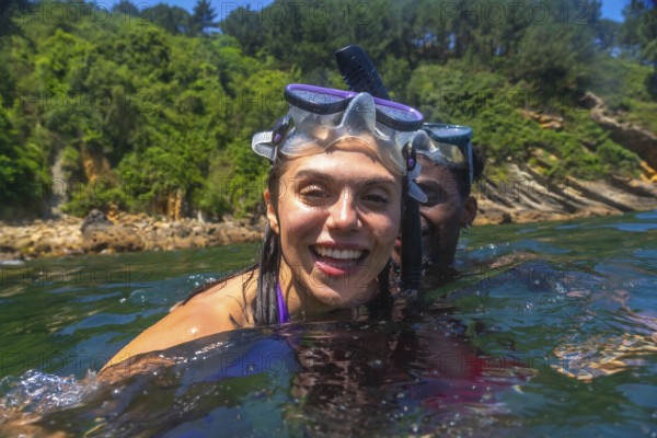 Interracial couple snorkeling together in the ocean, surrounded by a vibrant green coastline,