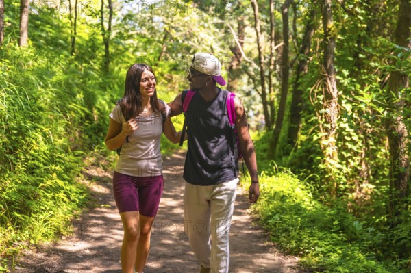 Interracial couple enjoying a hike on a forest path, wearing backpacks and casual clothes, engaging