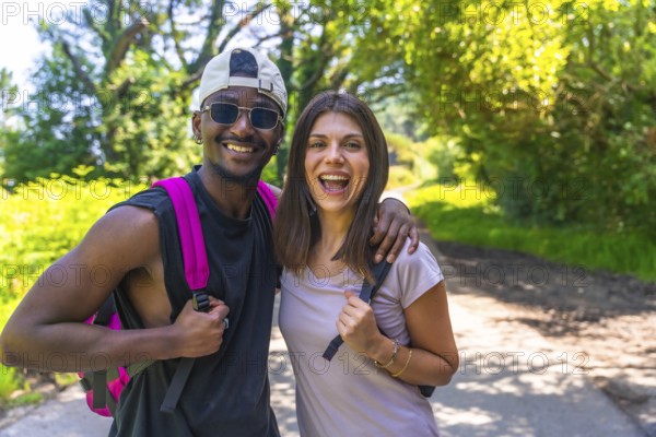 Interracial couple hiking on a sunny summer day, embracing each other and sharing joyful smiles