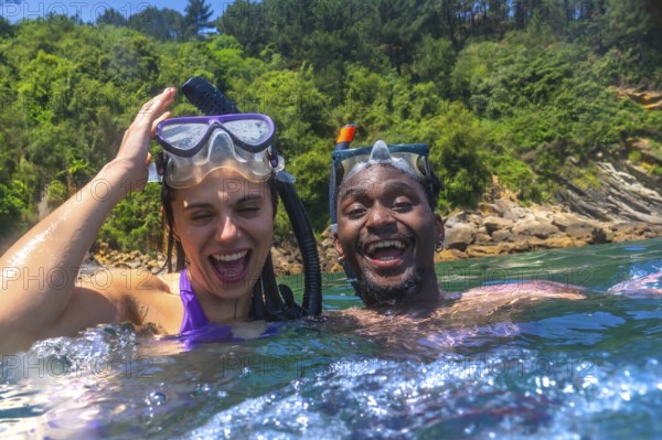 Interracial couple enjoying a fun snorkeling adventure in the vibrant ocean, laughing and sharing