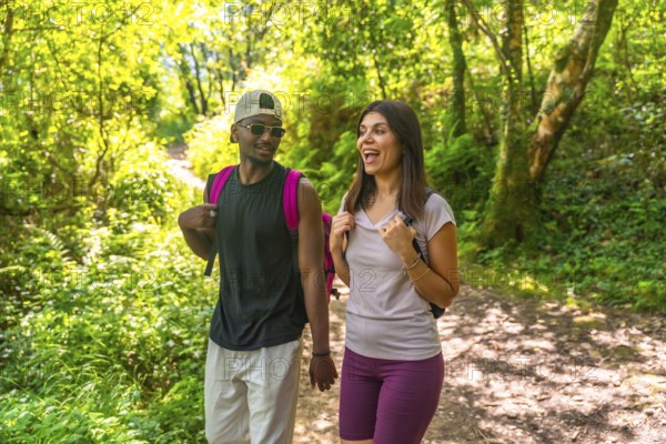 Interracial couple of hikers enjoying a conversation while walking on a trail in a lush green