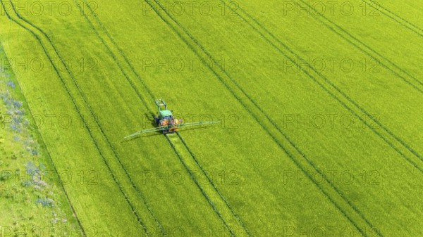Farmer with tractor working in the field. In early summer, he fertilises the grain for an optimum
