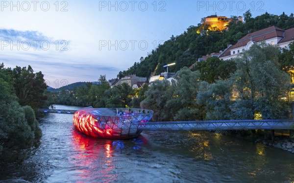 Night-time view of the Murinsel floating island on the river Mur with Schlossberg castle hill in