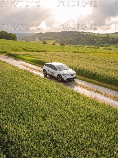 A car drives on a dirt track through a rape field under a cloudy sky, Deer E- CarSharing, Renault