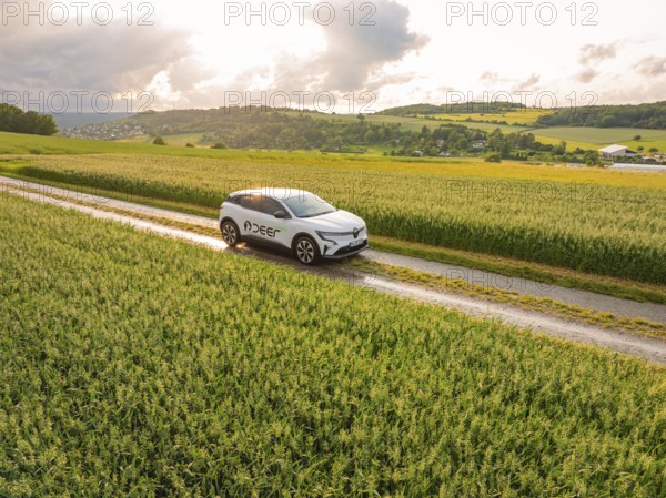 A car moves along a path through green fields with a wide view of the landscape, Deer E-