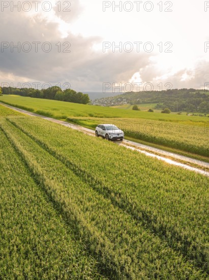 A car drives on a narrow road along green fields under a cloudy sky, Deer E- CarSharing, Renault