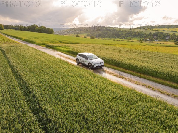 A modern car on a path through agricultural fields under a cloudy sky, Deer E- CarSharing, Renault