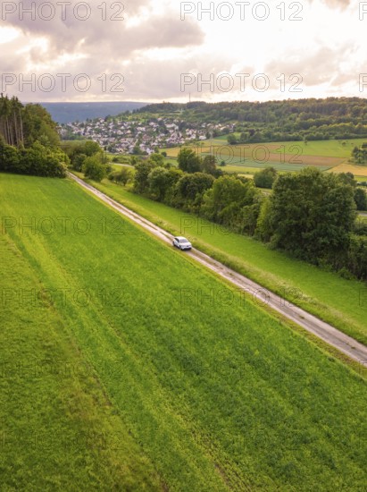Car on a long journey through green fields, hills and villages in the background, Deer E-