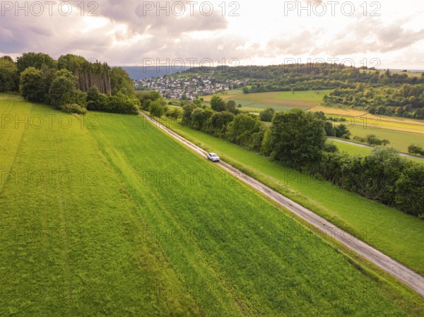 Car drives a straight road through wide green landscape with cloudy sky, Deer E- CarSharing,