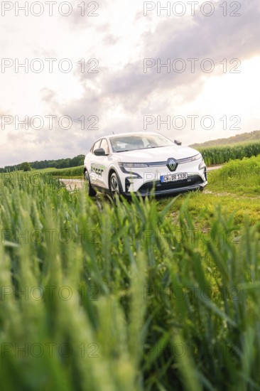 White car surrounded by vegetation and fields under a partly cloudy sky, Deer E- CarSharing,