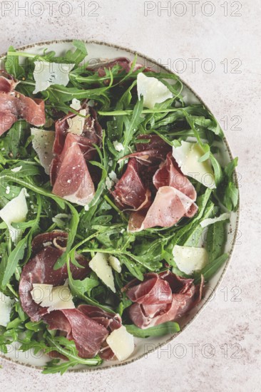 Fresh arugula salad with prosciutto and grated parmesan cheese, on a plate, homemade, no people