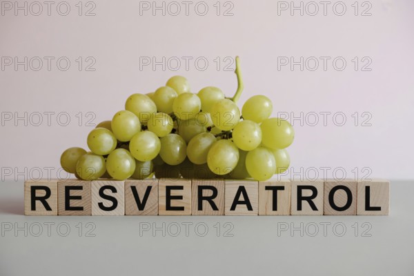 Fresh green grapes beside wooden blocks spelling Resveratrol. Clean studio image highlighting