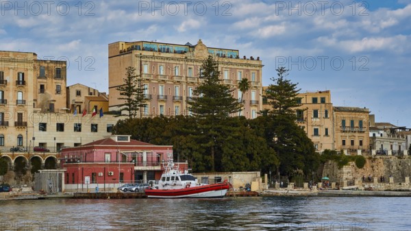 Boats in front of historic buildings and trees on a ponderous coast under a cloudy sky, boat trip