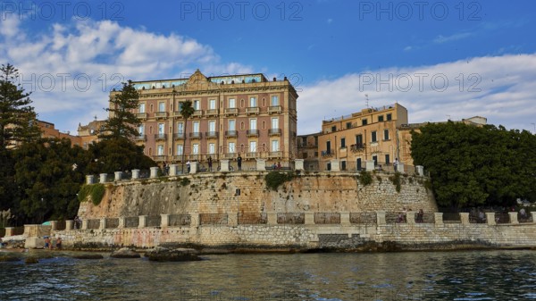 Elevated wall with historic buildings and lush vegetation in the coastal area, boat trip around the