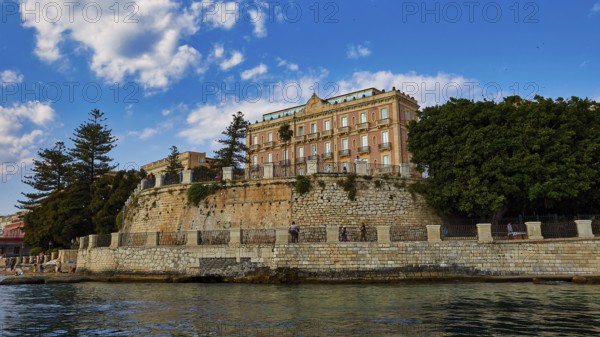 Magnificent building on a cliff, surrounded by lush vegetation and clear skies, boat trip around