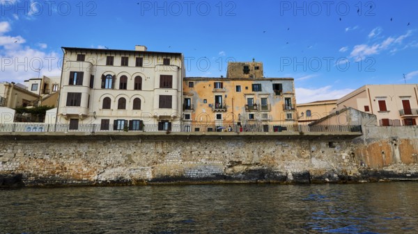 Historic buildings along a stone seawall under an expansive blue sky, boat trip around the island