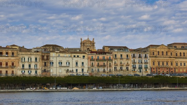 Rows of historic buildings along a coastal promenade under a patterned sky, boat trip around the