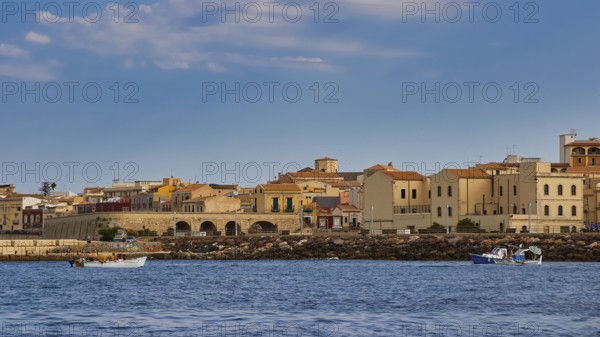 Town by the sea with old buildings and small boats, blue sky above, boat trip around the island of