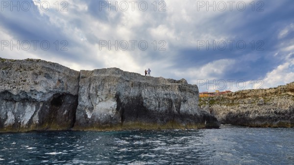 People standing on cliffs under a dramatic sky by the sea, boat trip around the island of Ortigia,