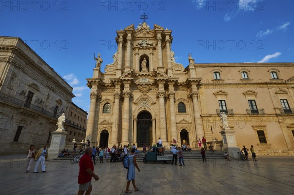 Cathedral of Syracuse, Large cathedral on a square with people and statues under a blue sky,