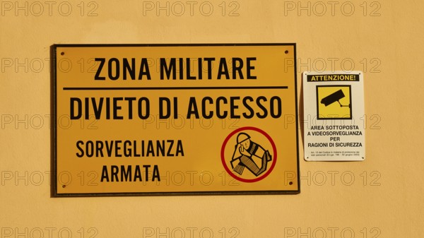 Warning sign on a wall indicating a military zone with restricted access and surveillance, Ortigia