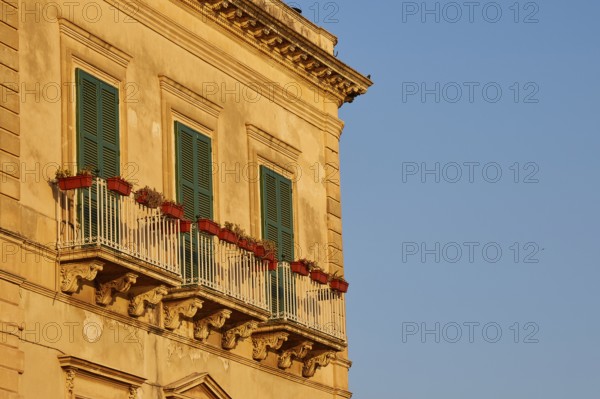 Facade of a building with balconies and green shutters in the sunlight, Ortigia Island, Isola di