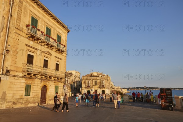 People and historic buildings on a sunny town square in the evening, Ortigia Island, Isola di