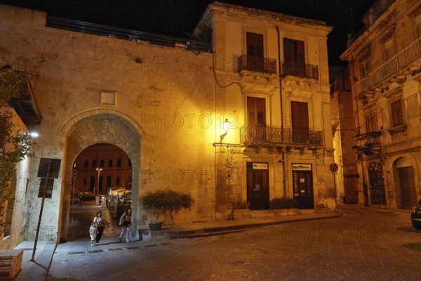 Night scene of an illuminated historic alley and a large gate with cobblestones and lantern light,