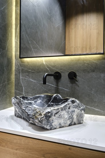 A unique stone sink made from natural rock rests on a sleek countertop in a modern bathroom. Soft
