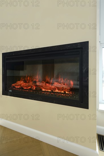 An electric fireplace is set into a wall in a bright living room. Flickering flames illuminate the