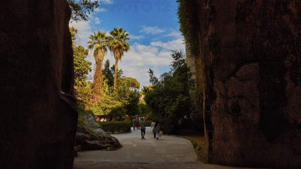 Cave Ear of Dionysus, Two people walking through a rocky passage with palm trees in the background
