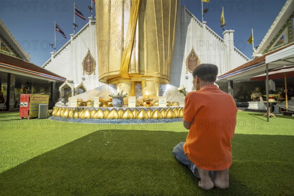 Man praying in front of a 32 metre high standing Buddha decorated with glass mosaics and 24 carat