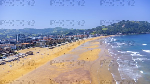 Aerial view of zarautz beach during a sunny summer day, featuring golden sand, blue water, and lush