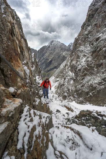 Mountaineer on a rope-secured path in a steep rocky mountain landscape with fresh snow in summer,