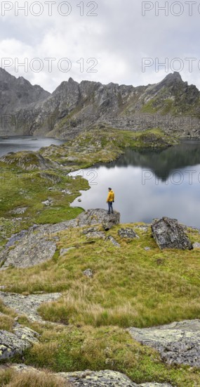 Mountaineer on a rock in front of mountain lakes Wangenitzsee and Kreuzsee, cloudy mountain peaks
