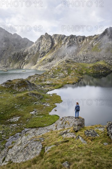 Mountaineer on a rock in front of mountain lakes Wangenitzsee and Kreuzsee, cloudy mountain peaks