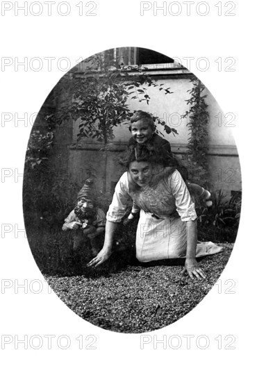 Woman carrying a child on her back, 1920s, A woman crawls on the floor with a child on her back,