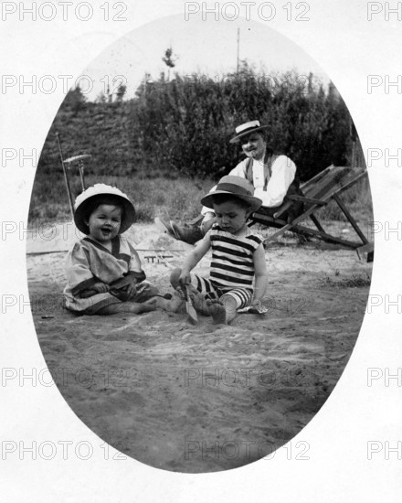 Father with 2 children beach deckchair, 1920s, Two children playing in the sand, an adult in the