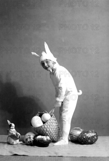 Girl dressed up as an Easter bunny, 1930s, A child in a bunny costume places a basket of eggs on