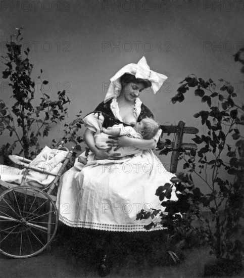Motherly love, mother breastfeeding baby, 1930s, mother breastfeeding baby next to a cart, black