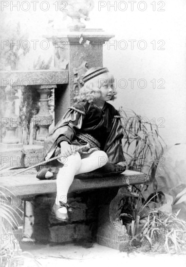 Dressed up girl with sword, 1930s, child in costume sitting on a stone bench, black and white scene