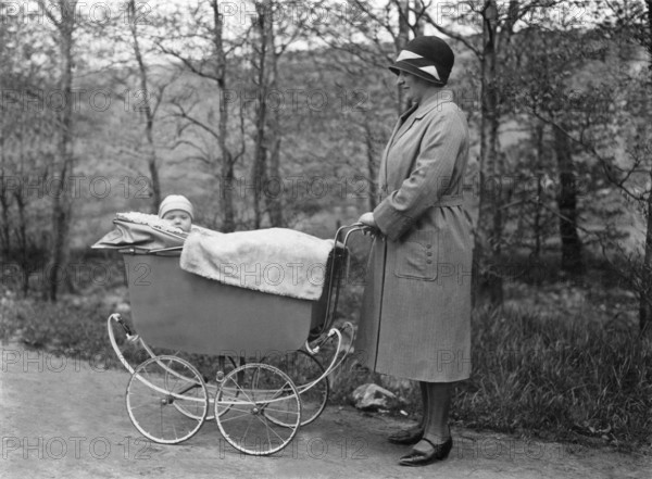 Woman pushing pram, 1920s, Woman with hat standing next to a pram and laughing with the baby lying