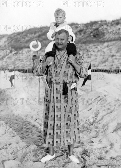 Man in bathrobe carrying child on shoulders, 1930s, A father carries his child on his shoulders on