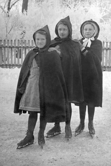 Three girls skating, 1930s, Three girls in hooded coats standing close to each other on an ice