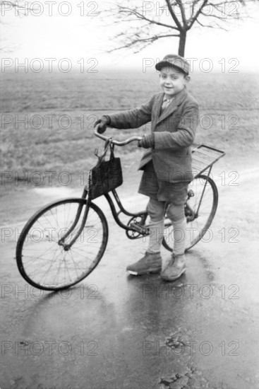 Boy with bicycle, 1920s, Boy standing with bicycle on a wet road in a rural environment, Historical