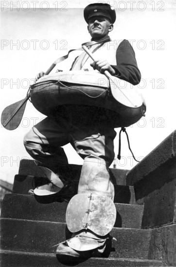 Man with boat and paddle 1940, A man in special rescue equipment stands on a staircase in front of