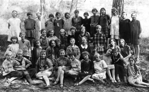 Girls class outing, 1930s, Large group of girls in school uniforms sitting outside in a wooded