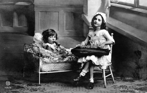 Two children making music, 1920s, Two girls, one in bed and one on a chair, playing in an old