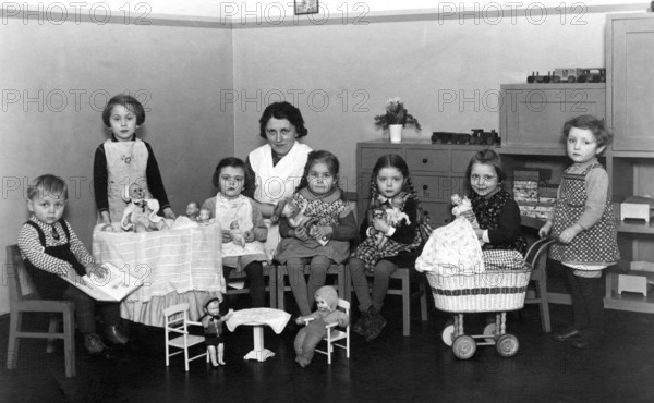 Kindergarten group toys, 1930s, children with woman in the room, playing with dolls and toys at a