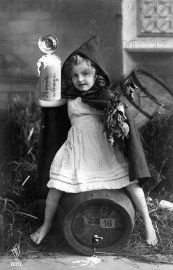 Girl drinking beer, ca. 1920, A girl with a hood is sitting on a barrel, holding an object in a